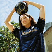 Female model wearing Kombat 2025 Modelo Soccer Jersey in navy blue and gold. Front view.