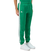 Man wearing Green Kappa track pants featuring Kappa Banda on side of legs in white and green. White Omini logo on right leg. Front side view.