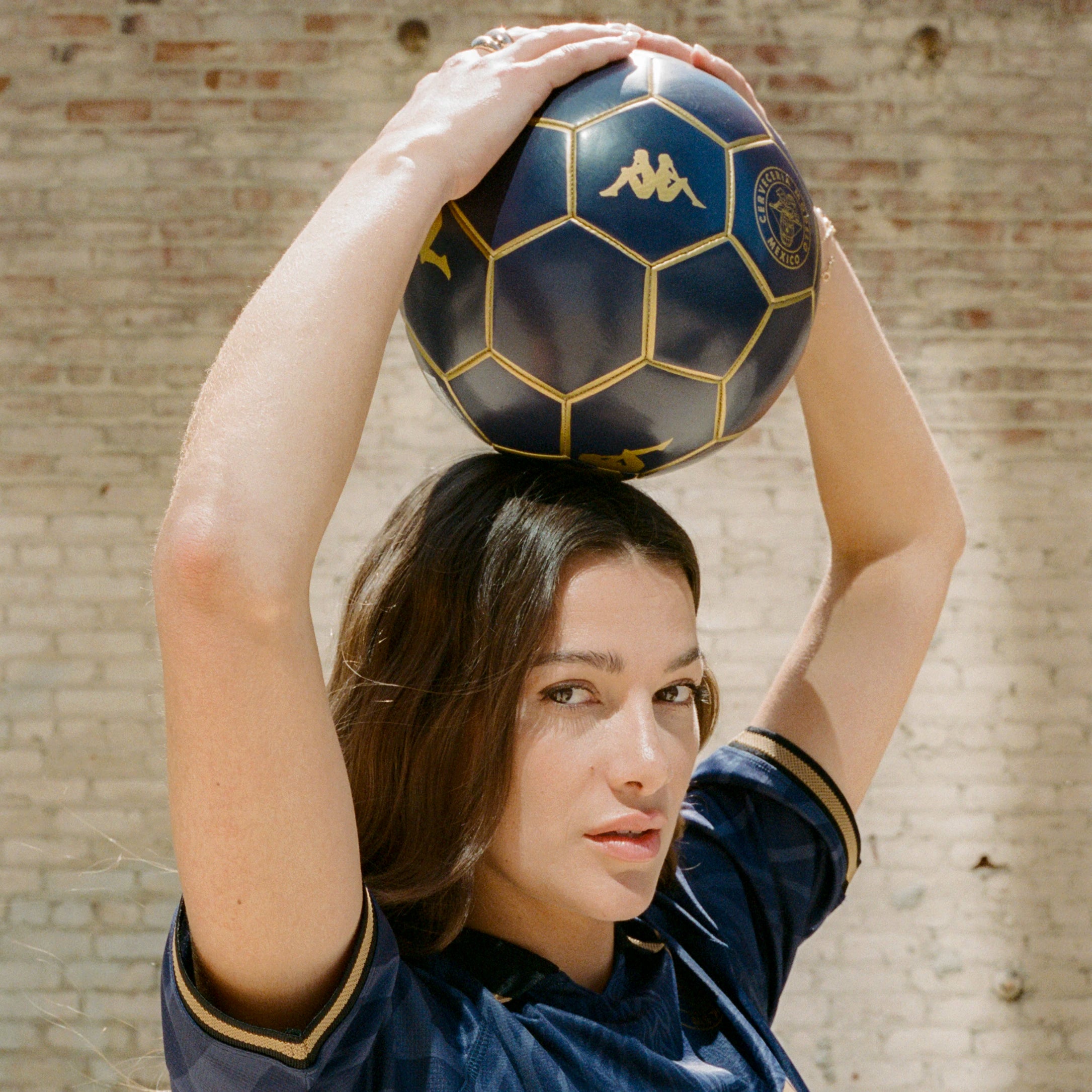 Female model holding Blasty Modelo Soccer Ball in dark blue with gold details showing Modelo and Kappa logos.