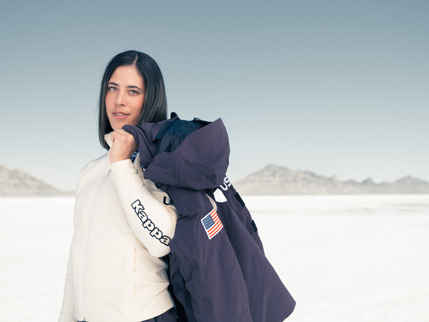 US Athlete poses on the salt flats wearing Kappa official US Ski and Snowboard Team Fleece holding Kappa US apparel over shoulder