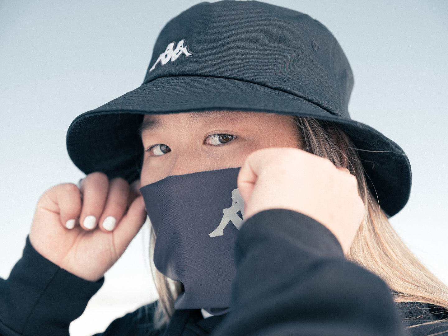 Close up of female US athlete wearing Kappa bucket hat pulling Kappa gator over her mouth and nose.