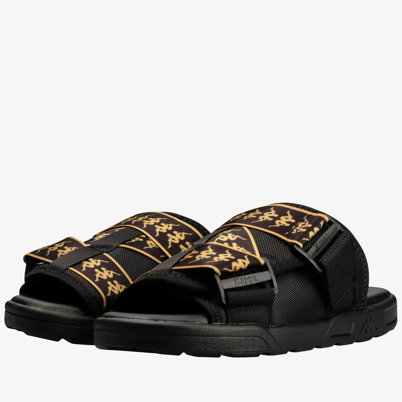 A pair of Kappa slide sandals in black with gold graphic patterns on the straps, shown against a plain white background.