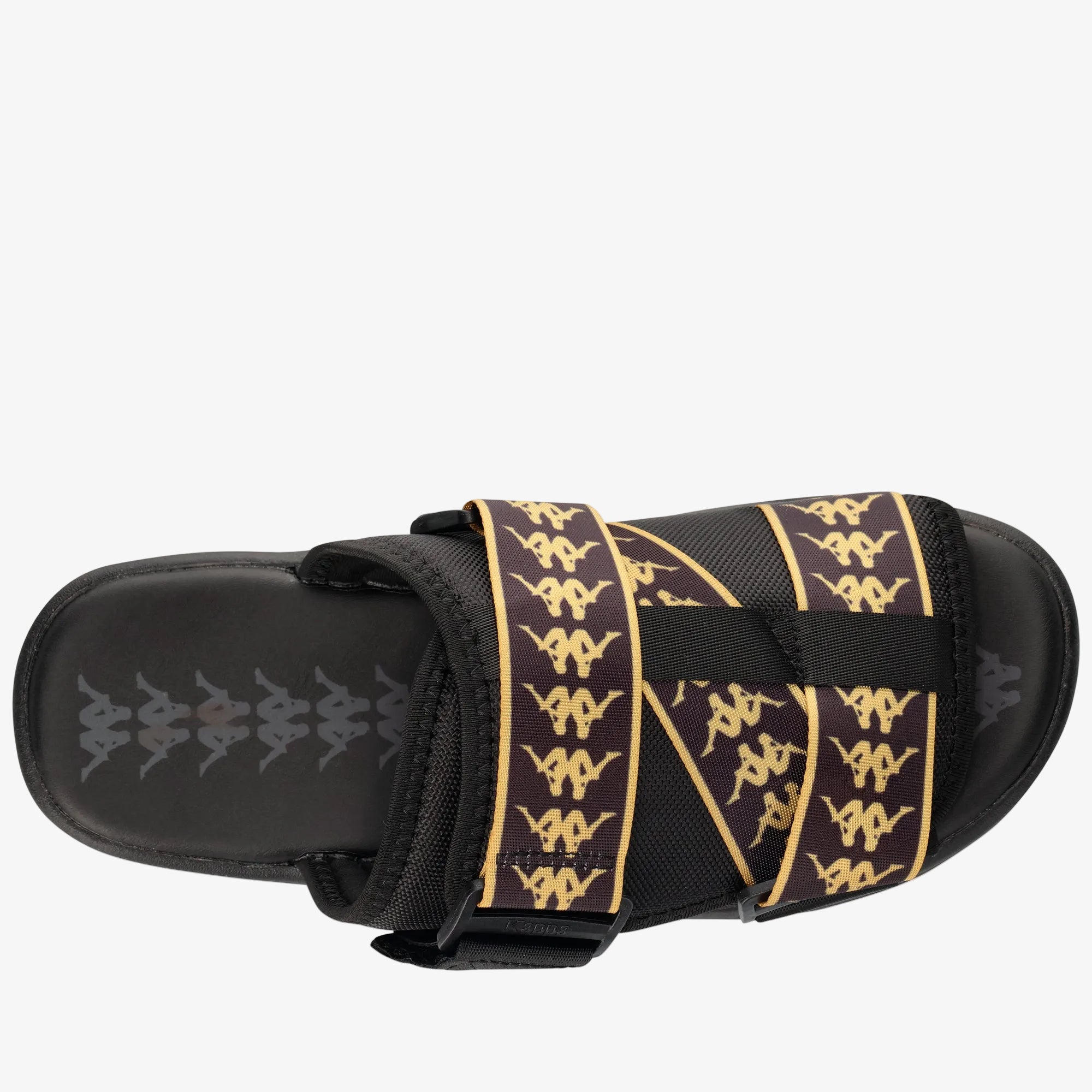A single Kappa slide sandal shown from a top-down view against a white background. The sandal features a black footbed and strap base with a wide, adjustable upper strap decorated with a repeating pattern of the Kappa logo in gold and black.
