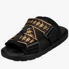 A black slide sandal featuring a wide adjustable strap with a black background and gold tribal-style snake graphics, shown on a white background.