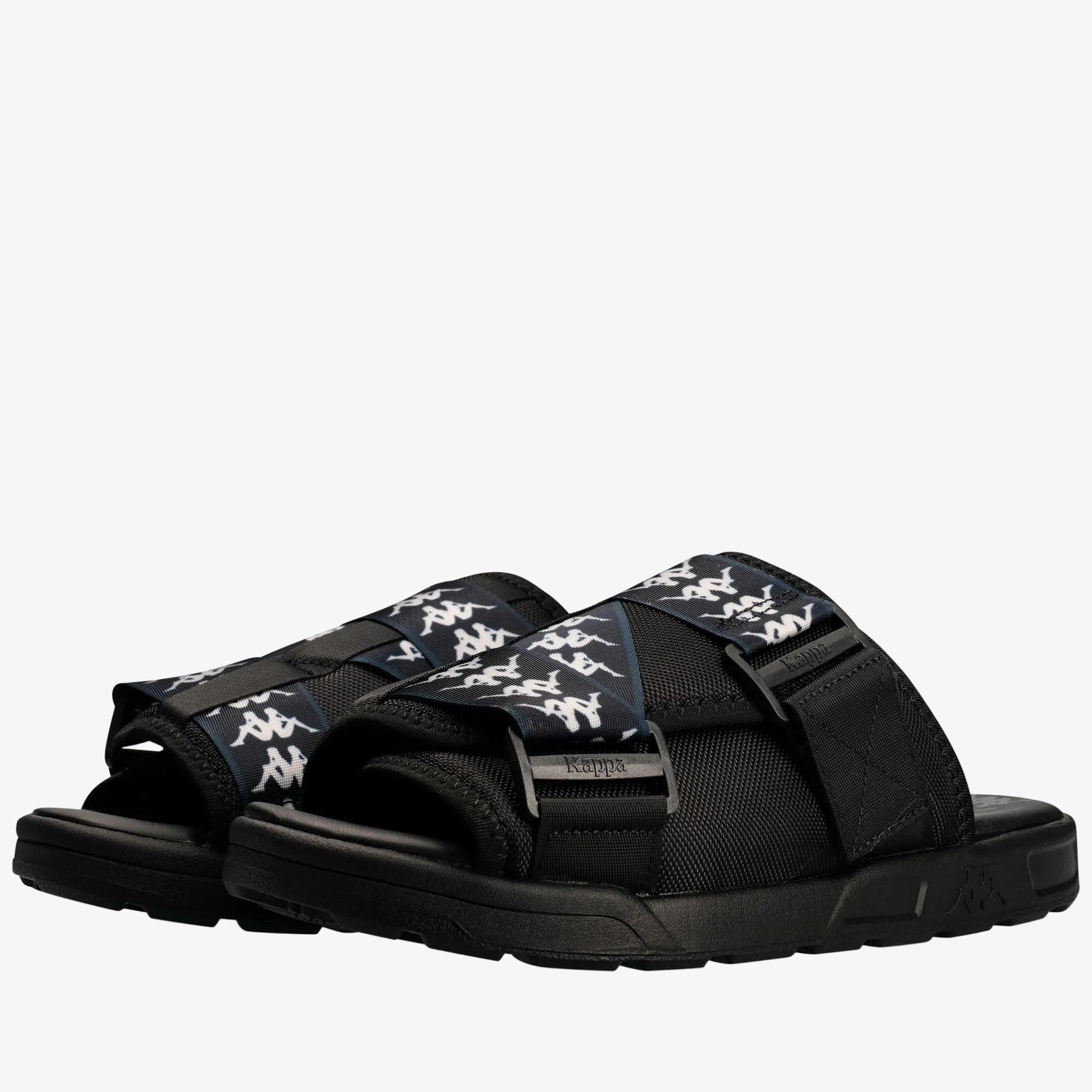 A pair of Kappa slide sandals in black with navy blue straps featuring the white Kappa logo pattern, shown on a clean white background.