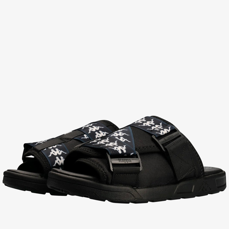 A pair of Kappa slide sandals in black with navy blue straps featuring the white Kappa logo pattern, shown on a clean white background.