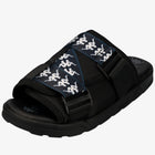 A black Kappa slide sandal with a wide black strap featuring a repeating white Kappa logo pattern, set against a plain white background.