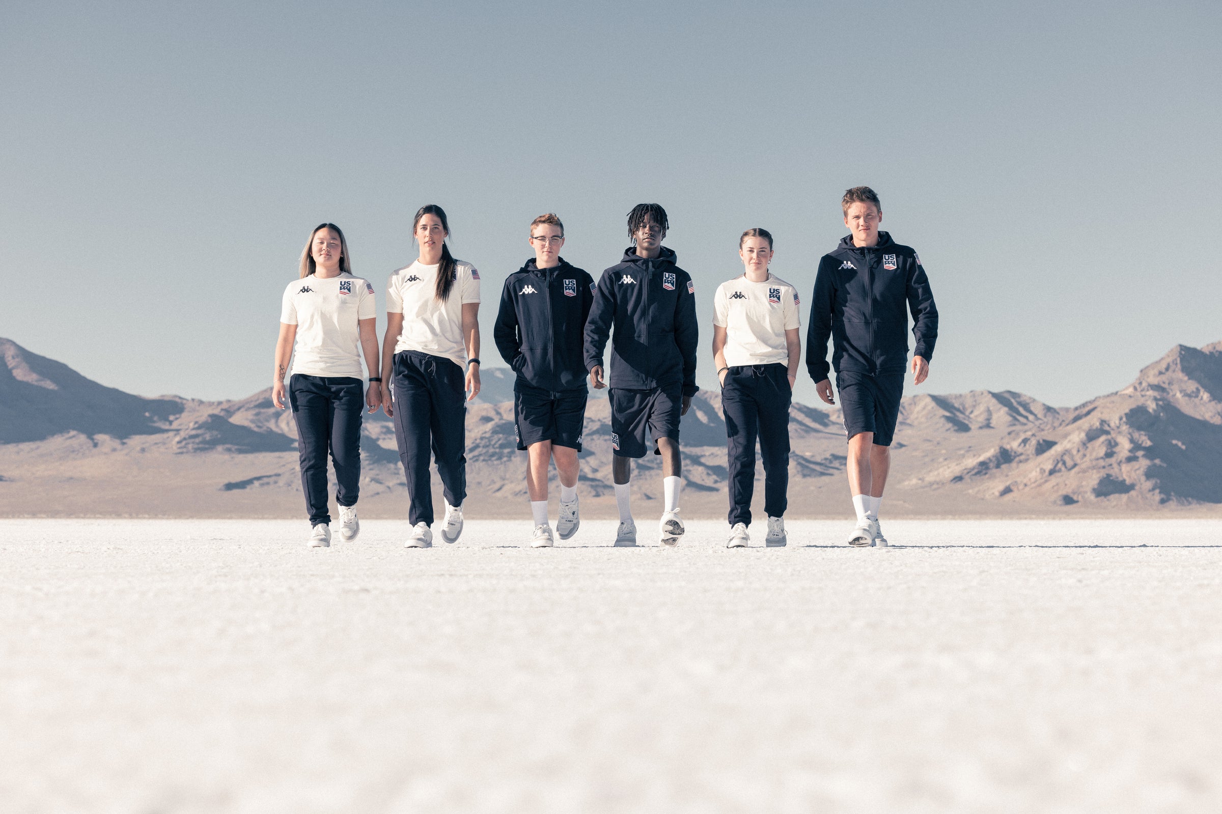 Group shot of six US athletes walking together in Kappa apparel on open salt flats.