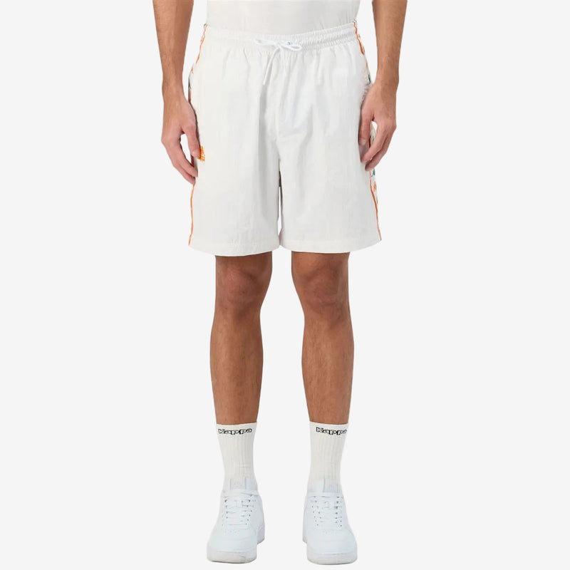 Man wearing white shorts featuring Kappa Banda on the sides with green and orange omini logos. Kappa Logo in Orange on right leg. Front view.