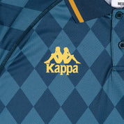 Blue checkered polo with gold detailing. Detail view of golden Kappa logo.