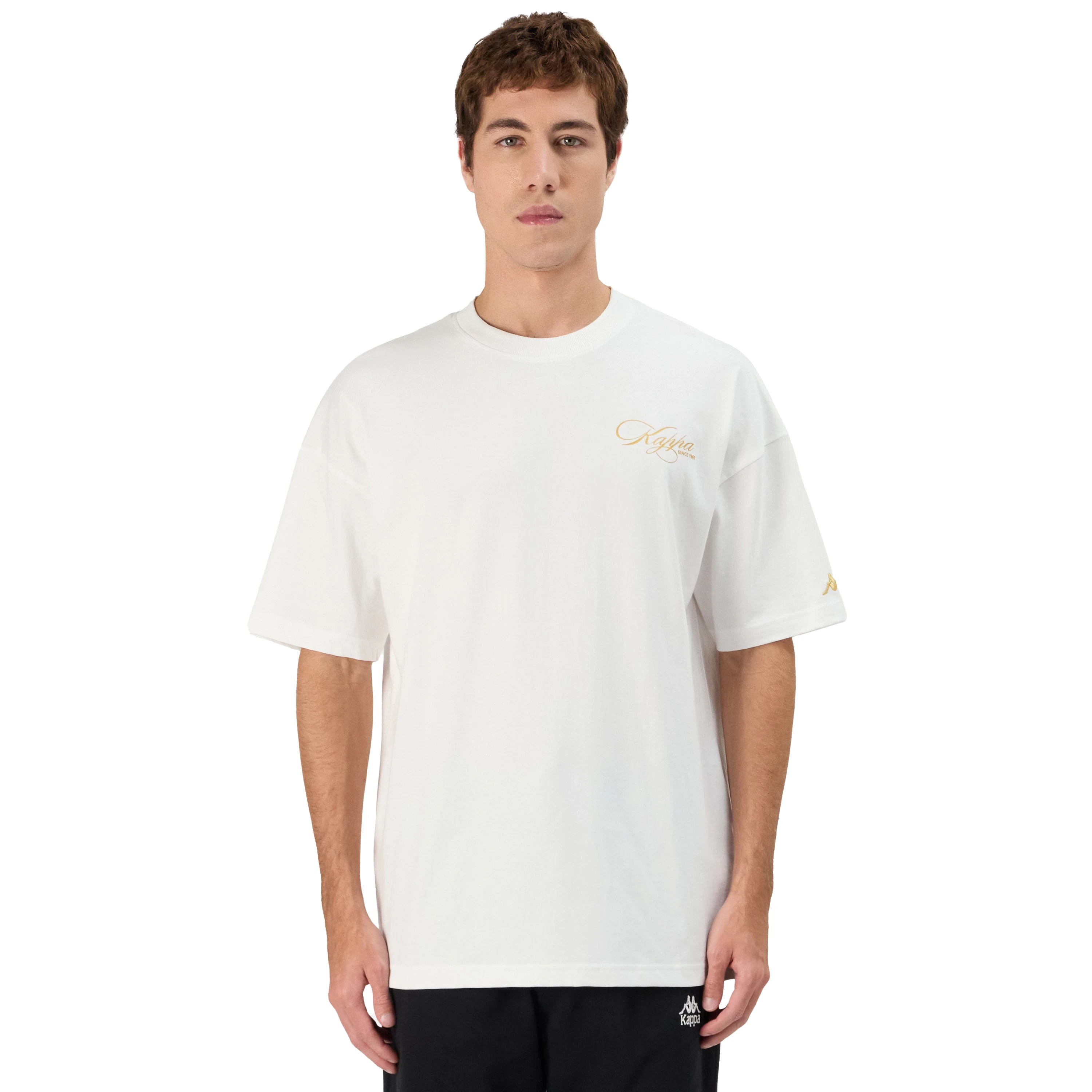 Man wearing white Kappa t-shirt with gold script on front left side and gold omini logo on left sleeve. Front view.