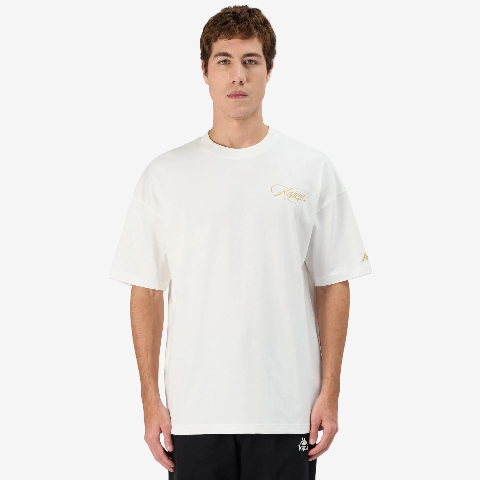 Man wearing white Kappa t-shirt with gold script on front left side and gold omini logo on left sleeve. Front view.