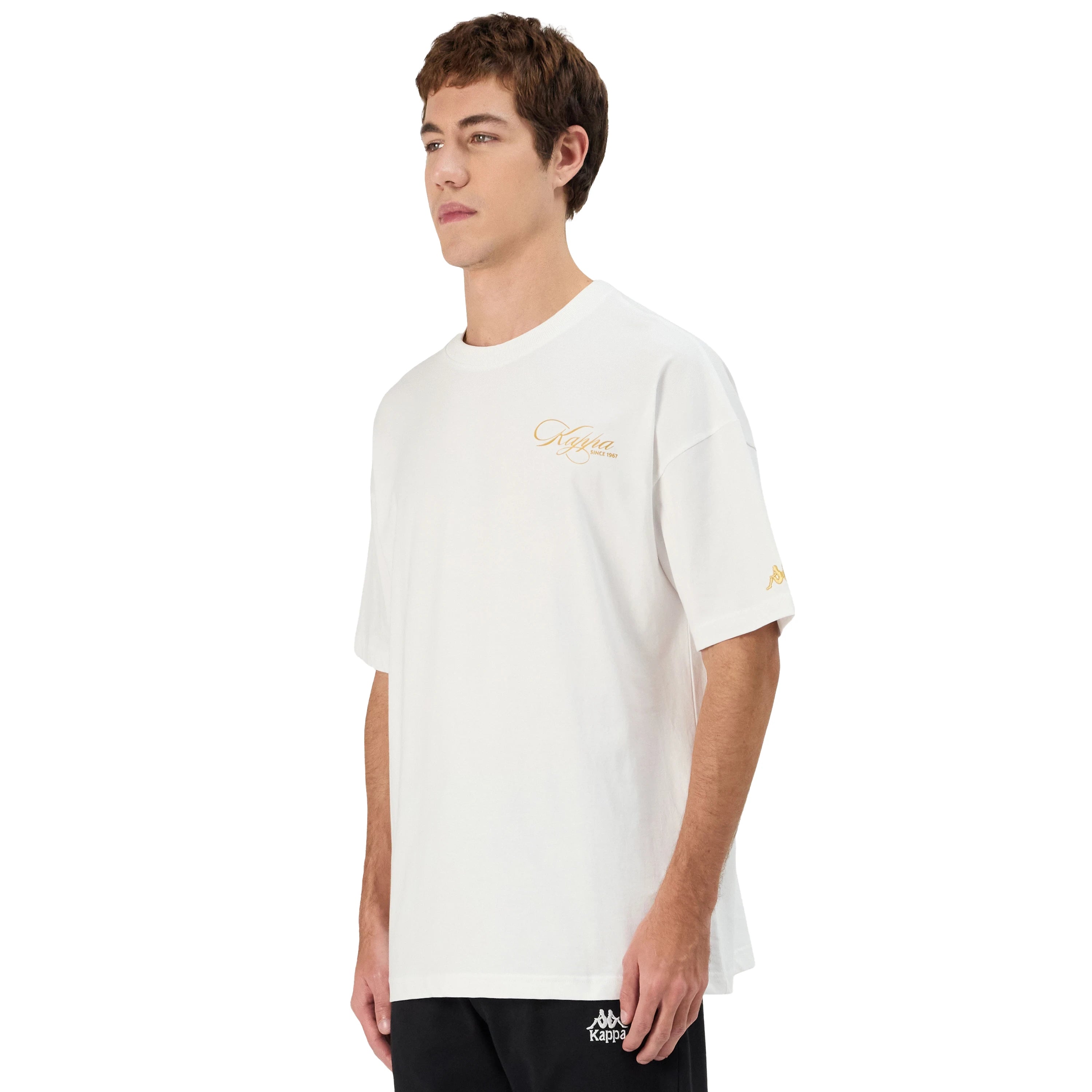 Man wearing white Kappa t-shirt with gold script on front left side and gold omini logo on left sleeve. Side view.