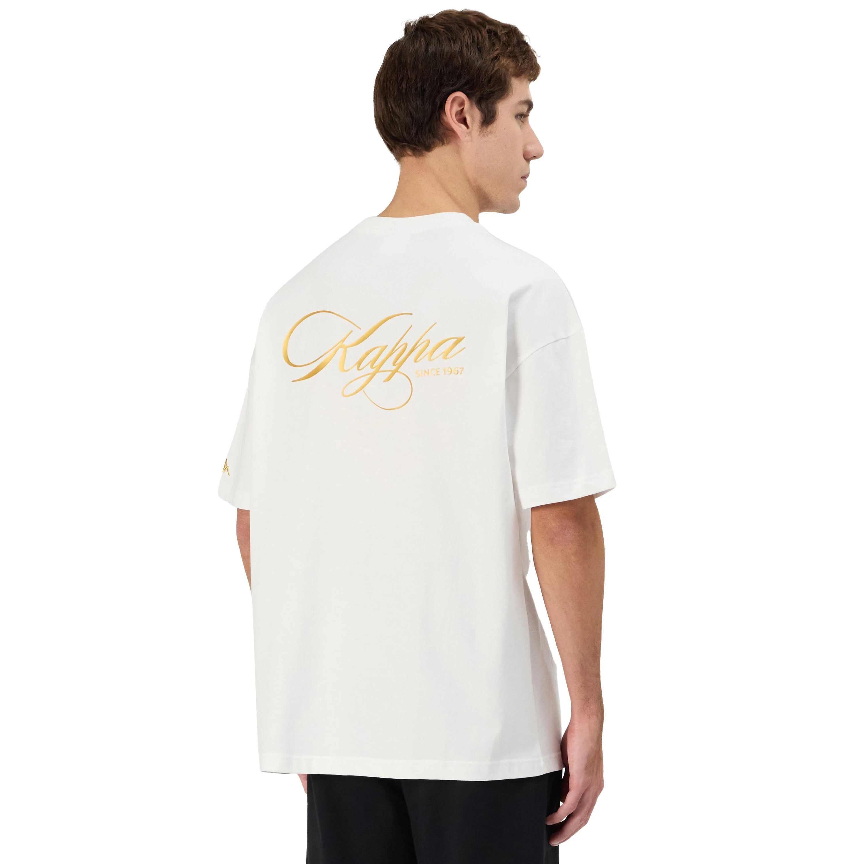 Man wearing white Kappa t-shirt with large gold script on back. Back view.