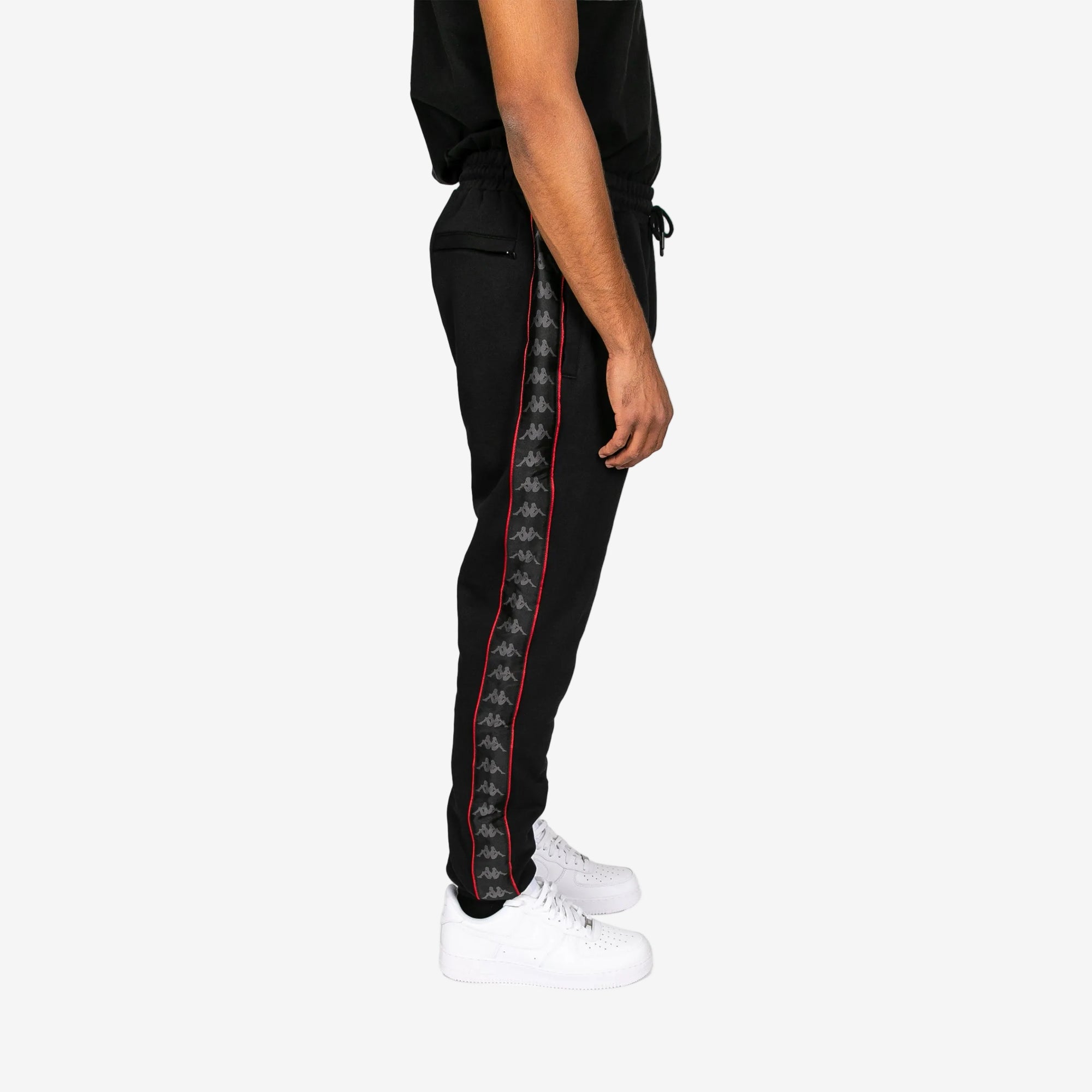 Black jogger pants with red and white striped side panels worn by a person on a white background