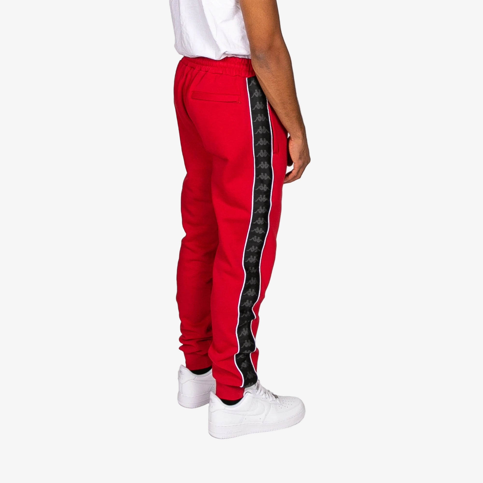 Red tracksuit pants with a black side stripe worn by a person on a white background