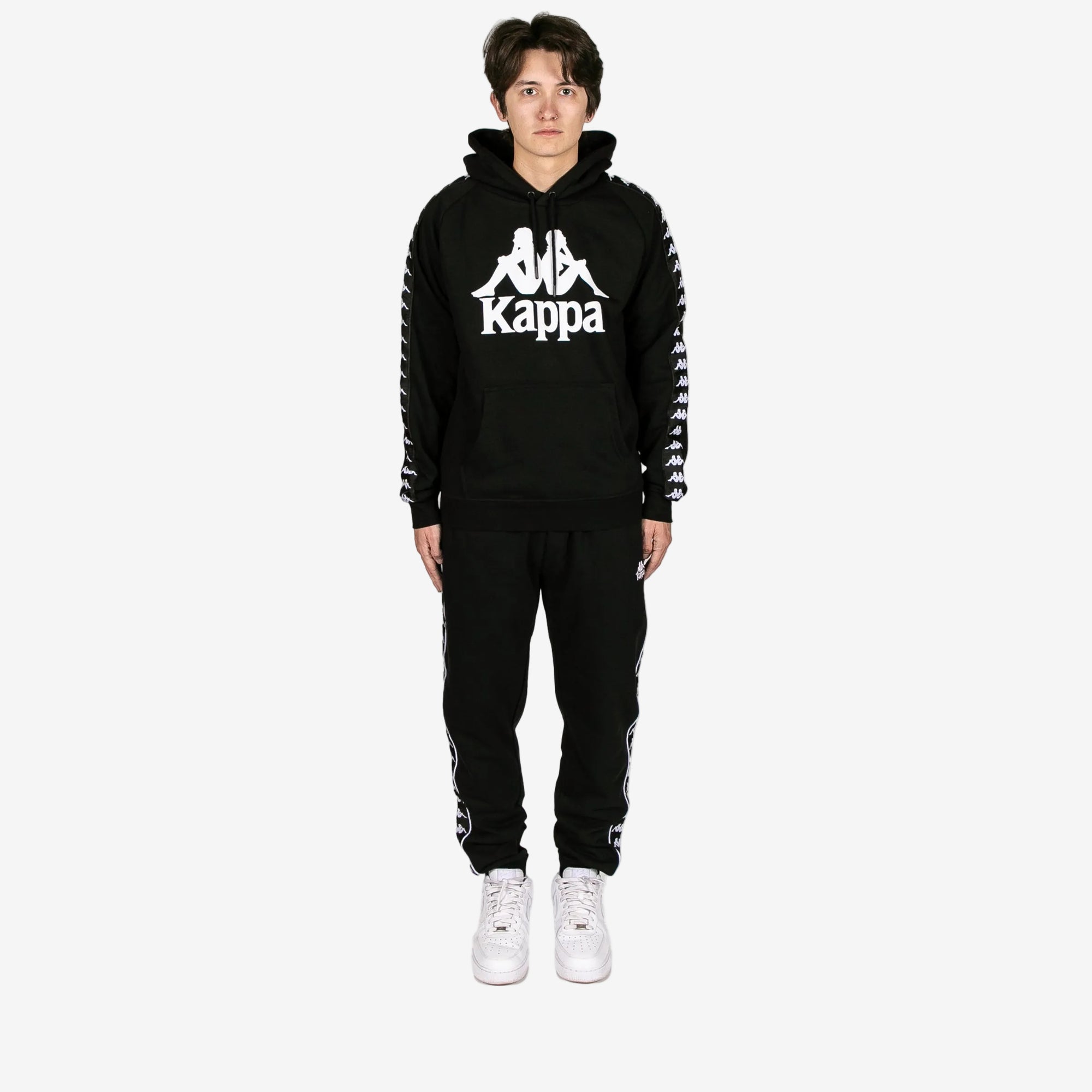 Person wearing a black Kappa tracksuit on a white background