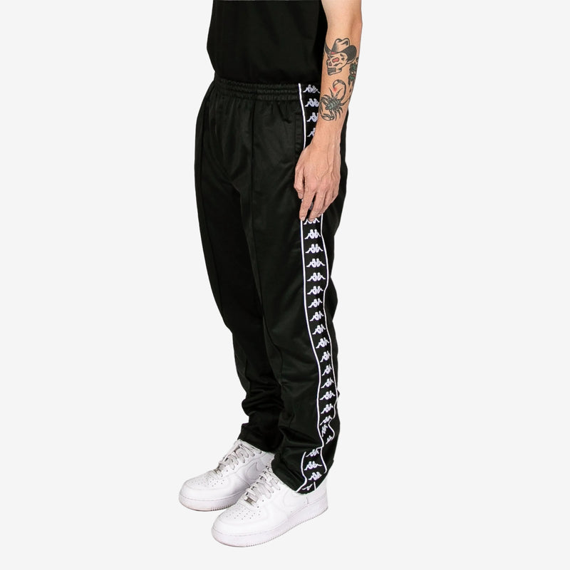 Black track pants with white logo stripe worn by a person on a white background