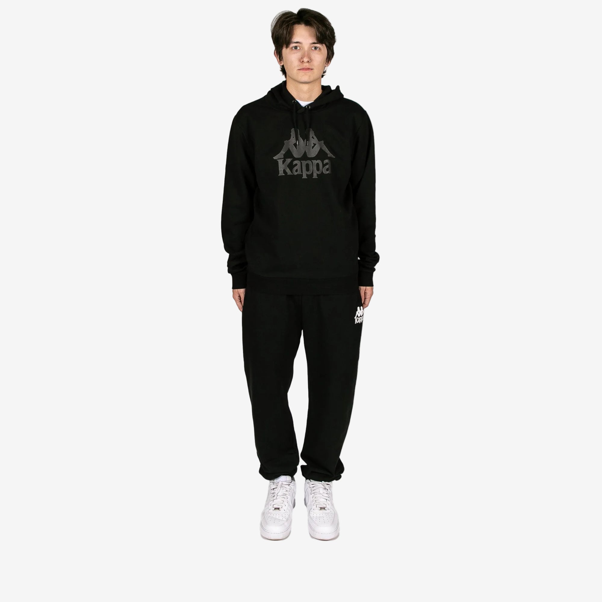 Person wearing a black Kappa hoodie and pants on a white background