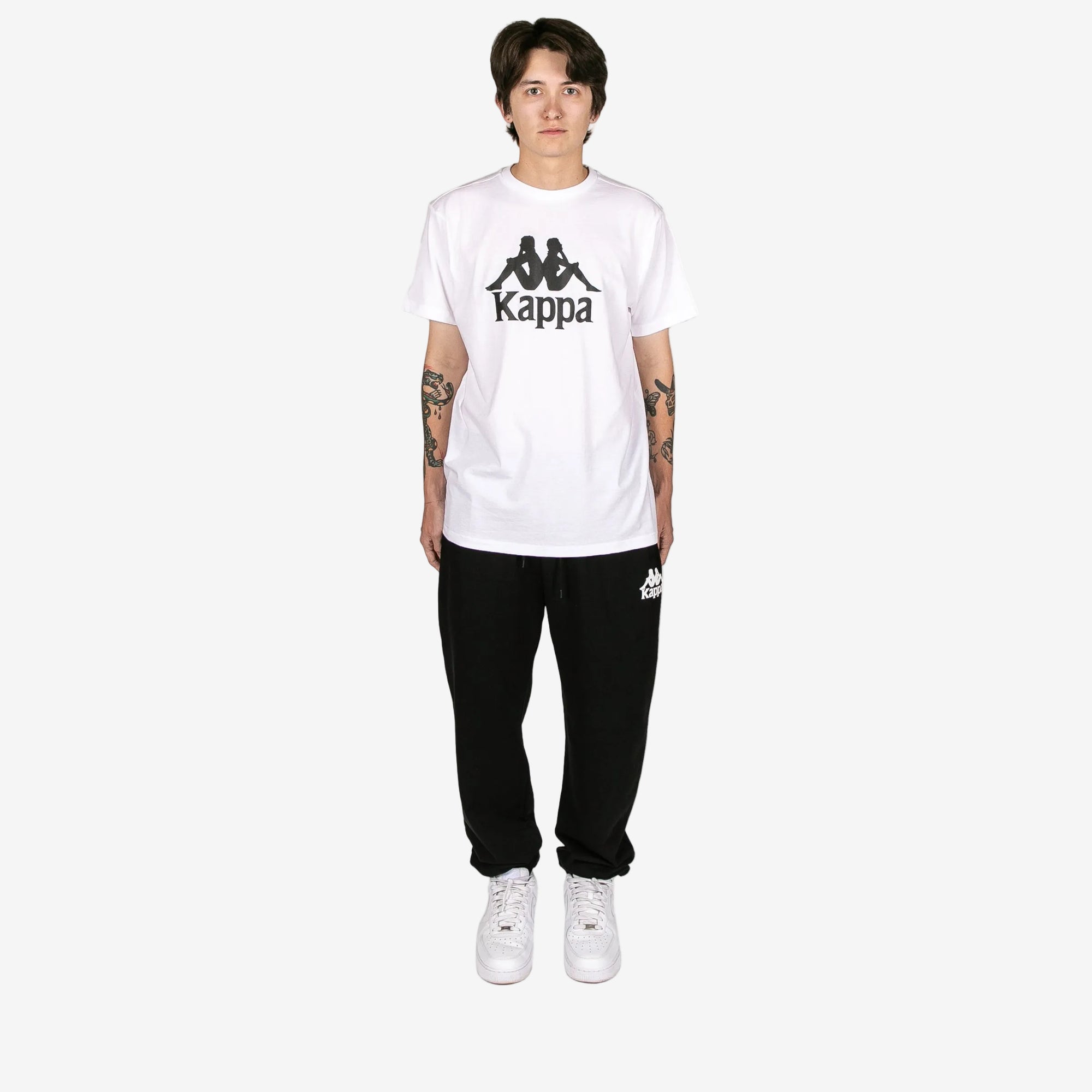 Person wearing a white Kappa t-shirt and black pants on a white background