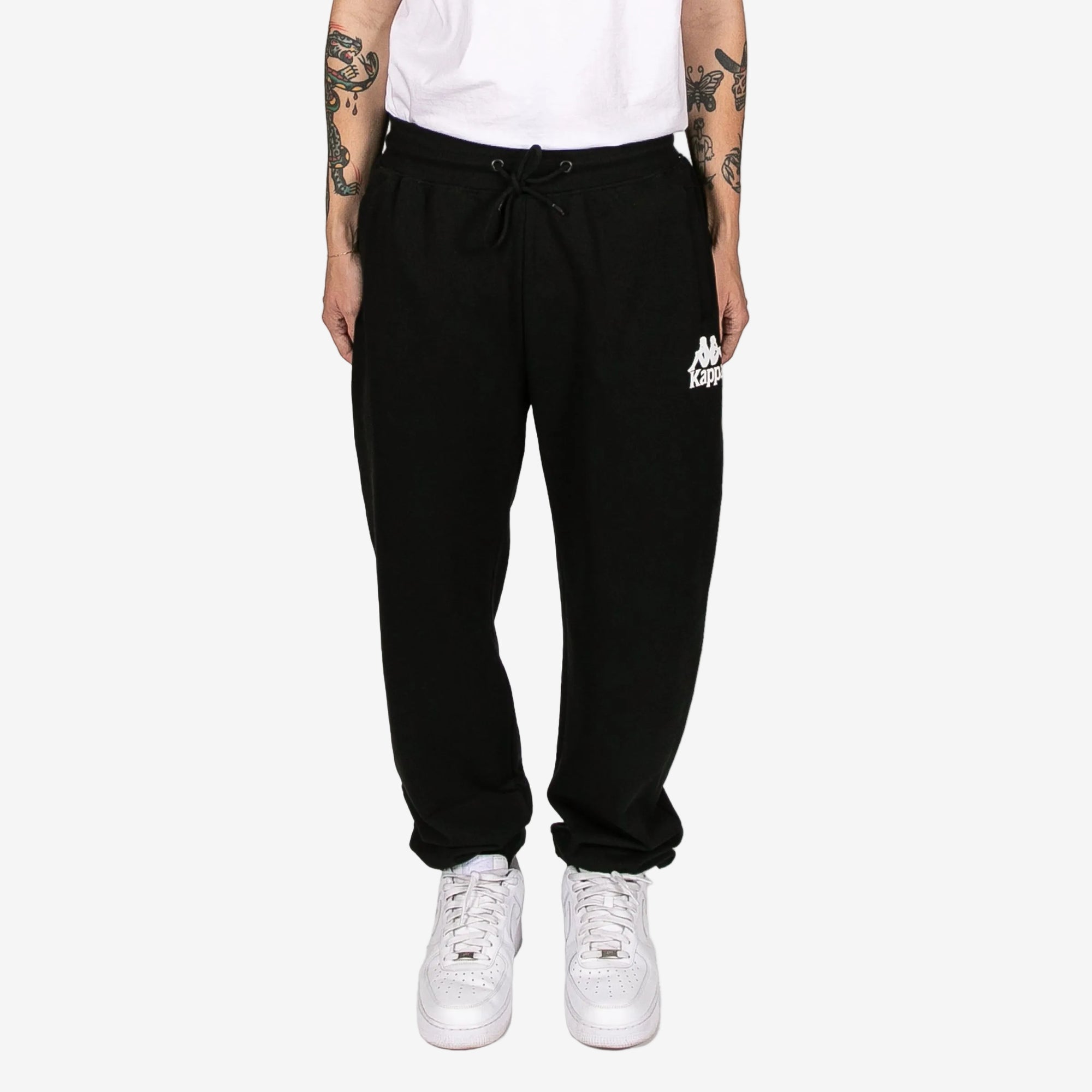 Person wearing black sweatpants with a logo and white sneakers on a white background