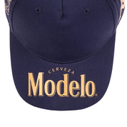 Close up of navy blue cap bill with Modelo logo in gold on the bill.