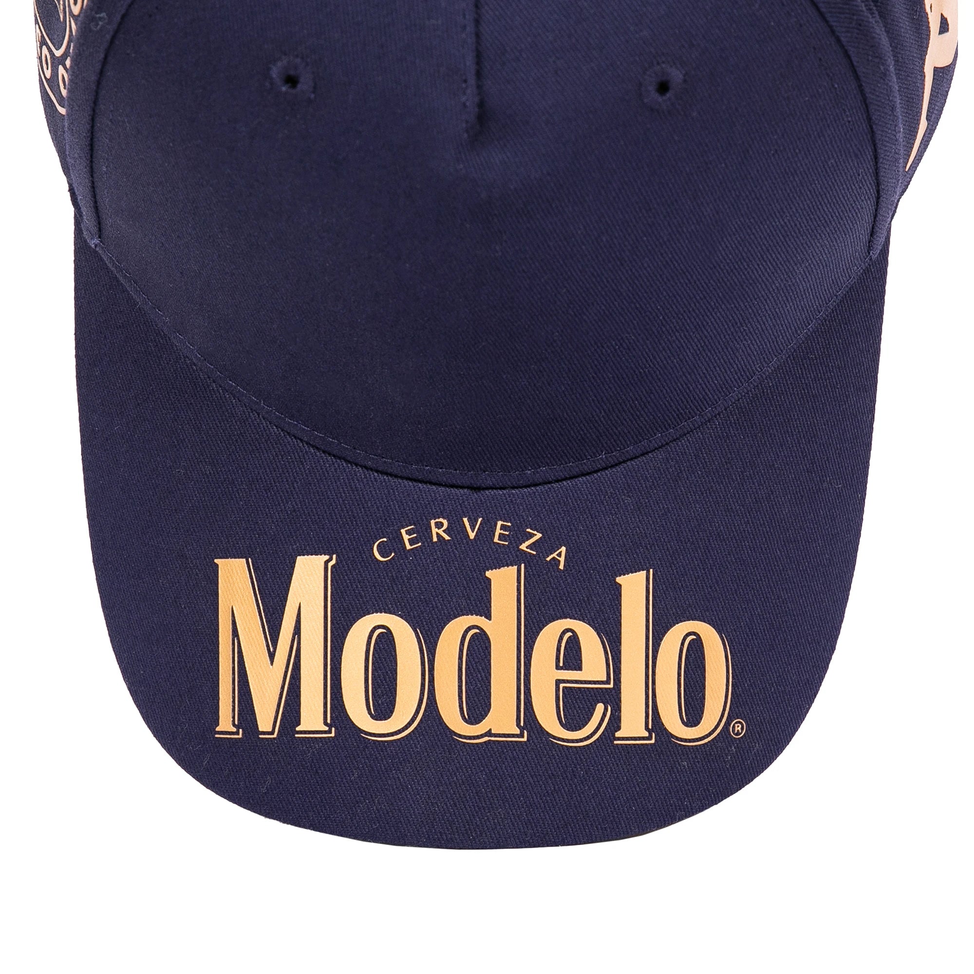 Close up of navy blue cap bill with Modelo logo in gold on the bill.