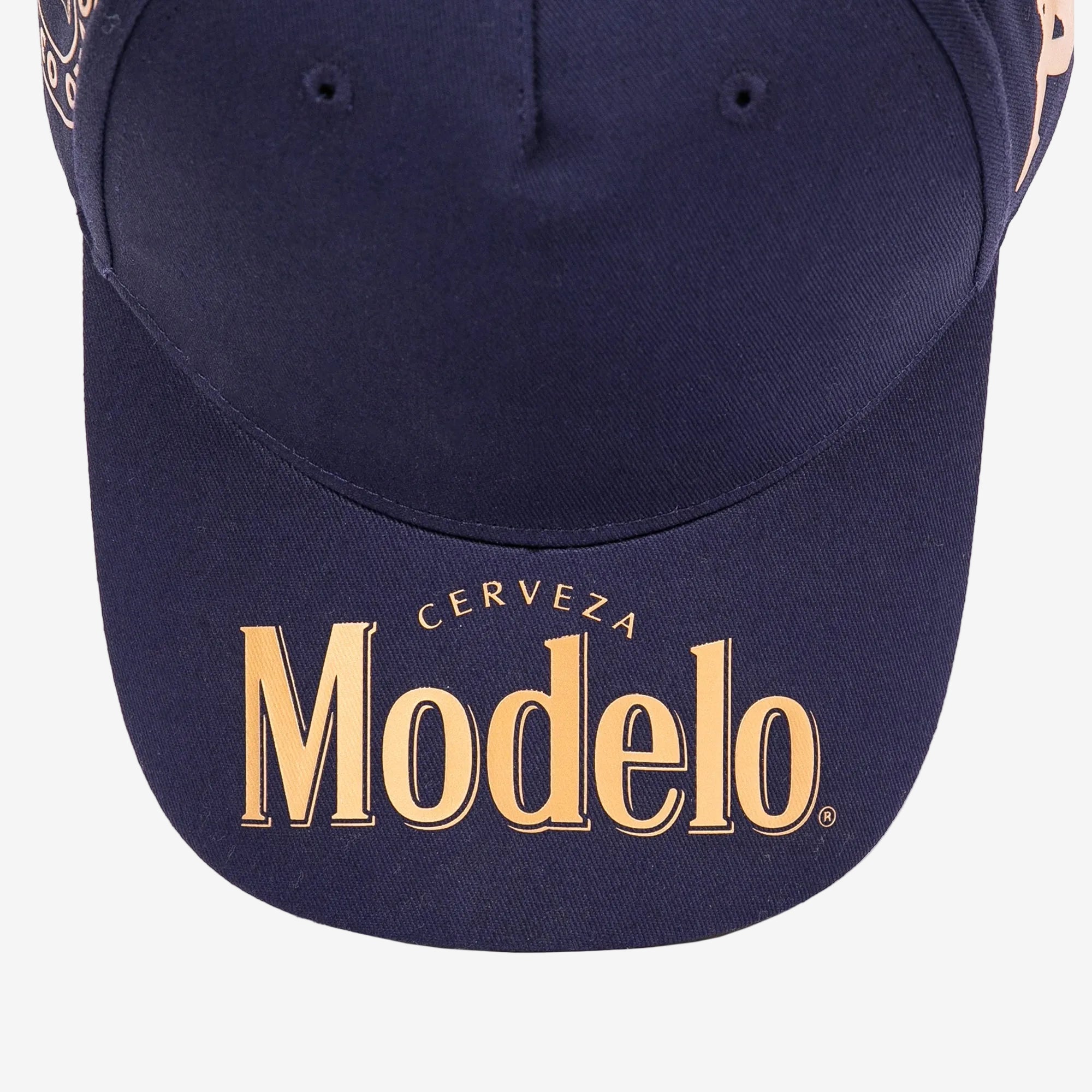 Close up of navy blue cap bill with Modelo logo in gold on the bill.