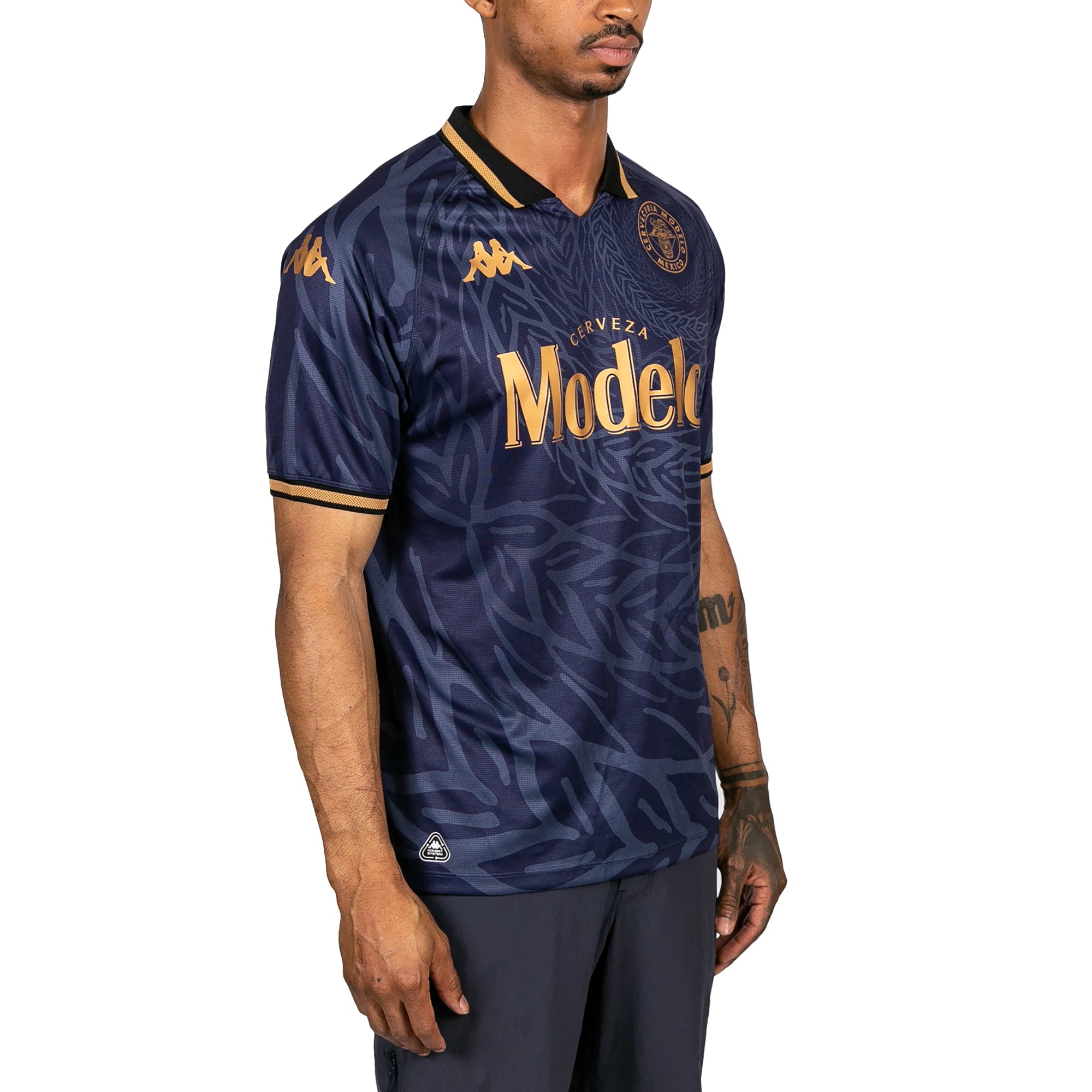 Male model wearing Kombat 2025 Modelo Soccer Jersey in navy blue and gold. Side view.